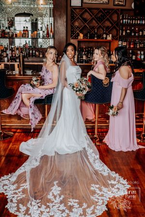 Wedding party gathered at rustic bar with elaborate bridal gown featuring long lace train and floral bouquets.