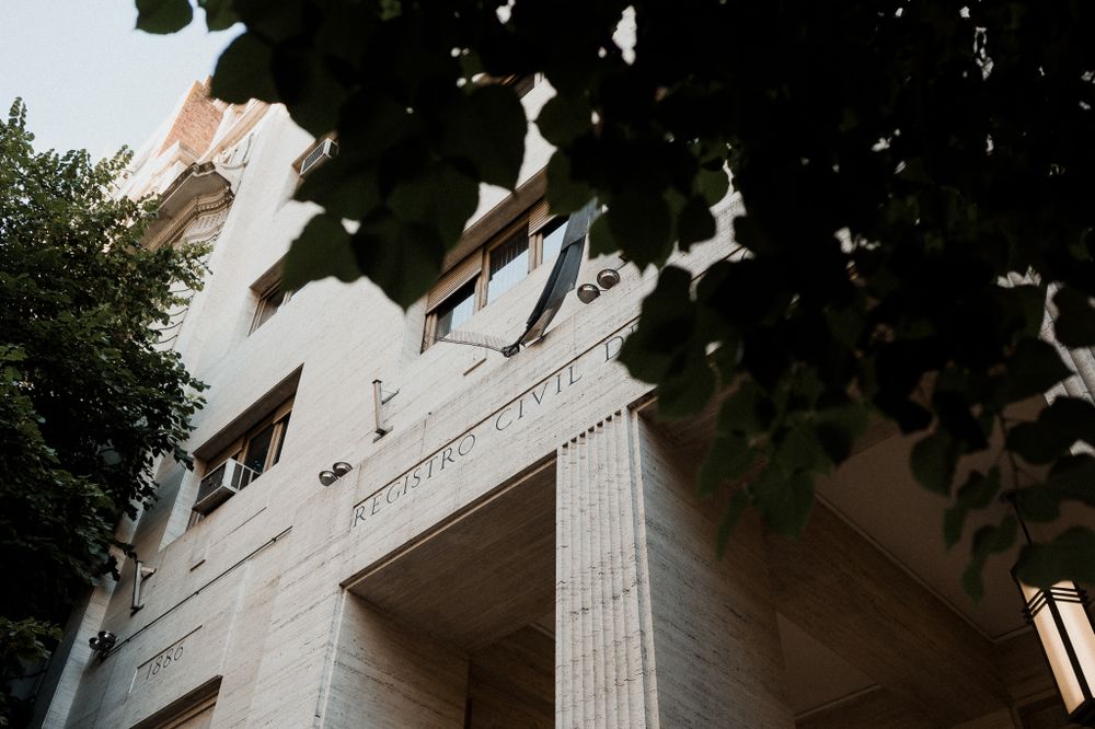 Low angle architectural shot of a white building facade with columns and windows framed by leaves.