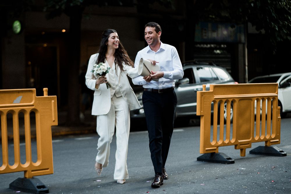 A couple in stylish monochromatic outfits walking together on a city street with orange barriers visible.