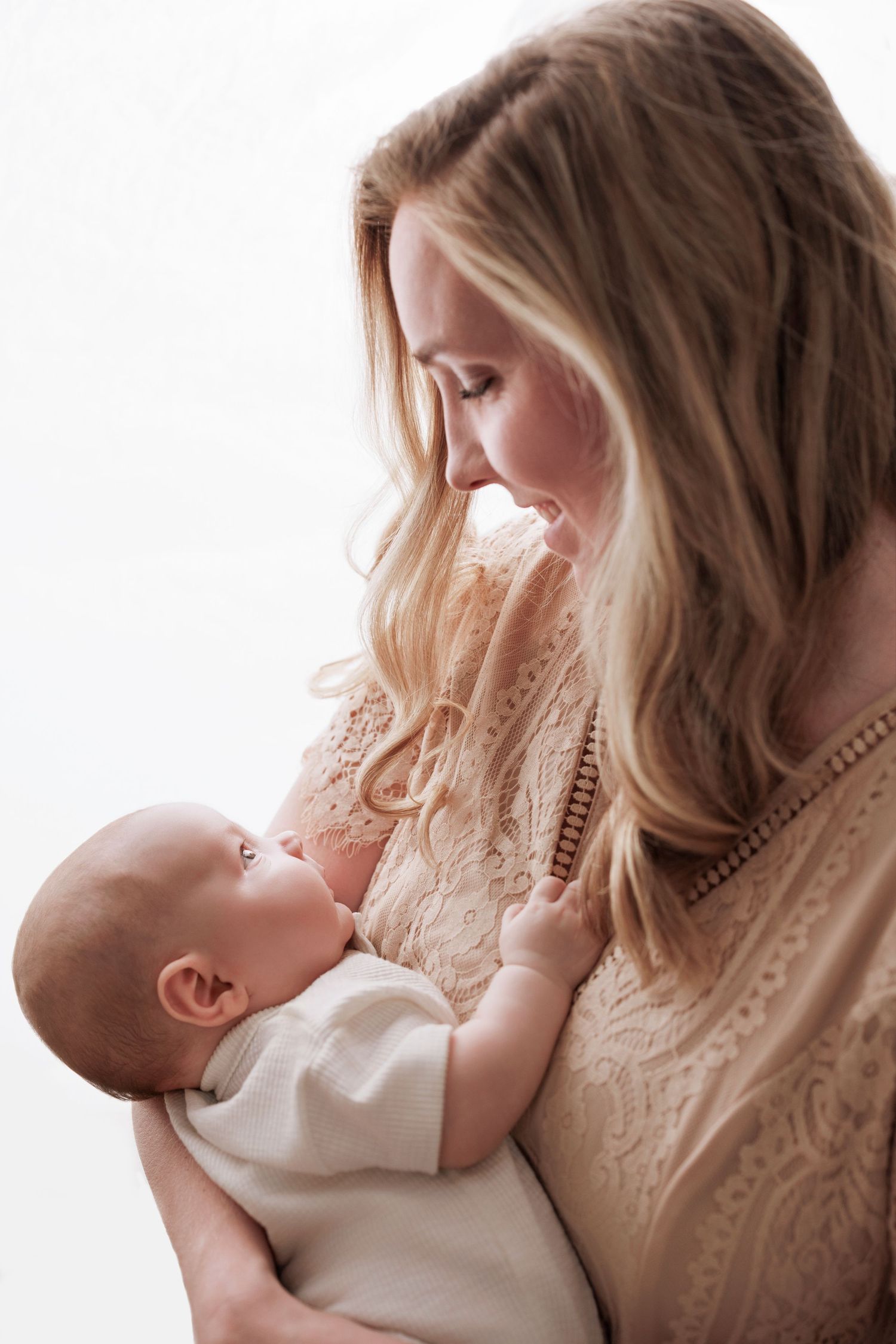 A tender moment between mother and newborn baby in soft natural light against white background.