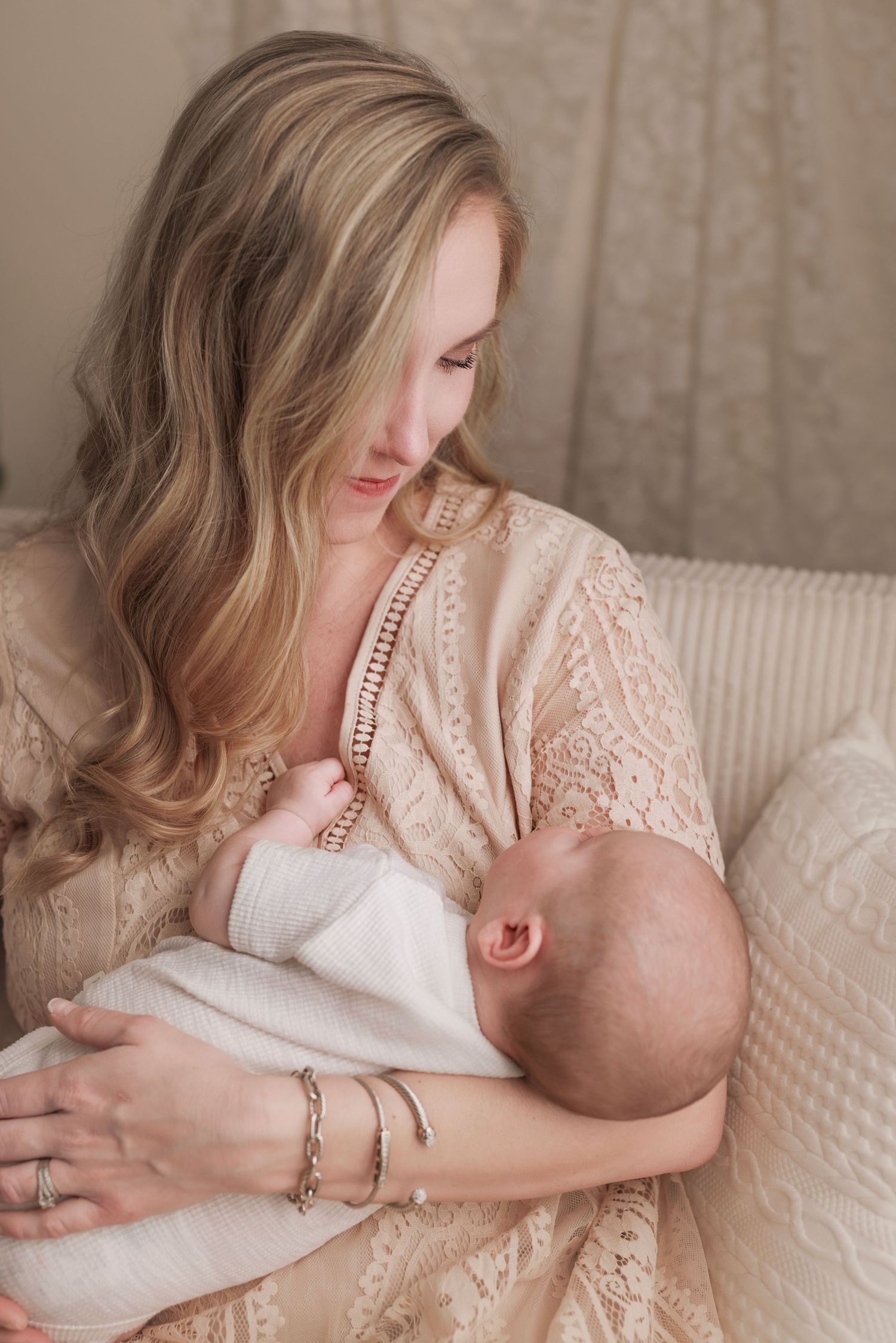 A tender moment between mother and baby as they cuddle together on a couch, wearing delicate beige lace.