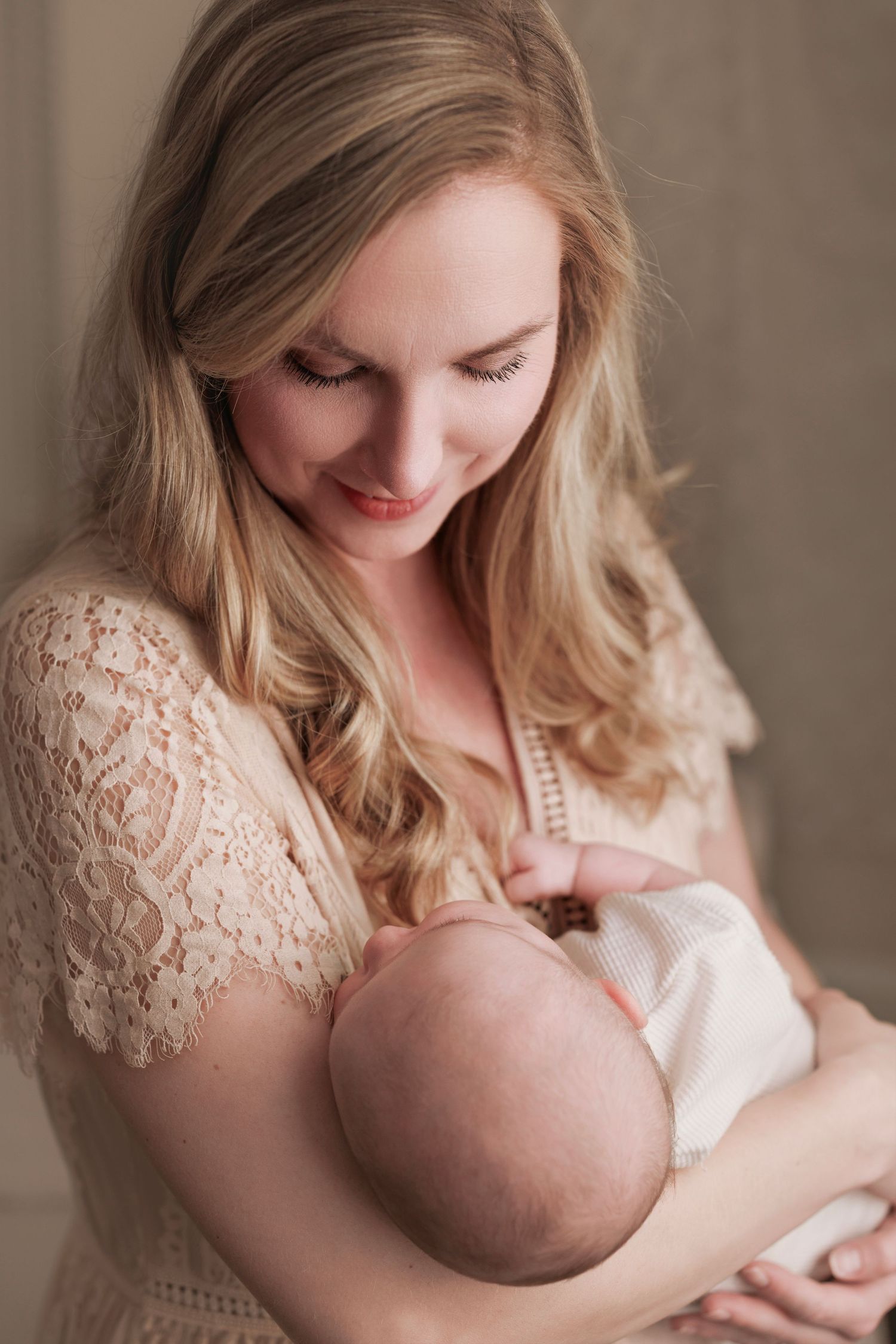 Intimate moment as mother in delicate lace dress cradles and nurses newborn baby with gentle expression.