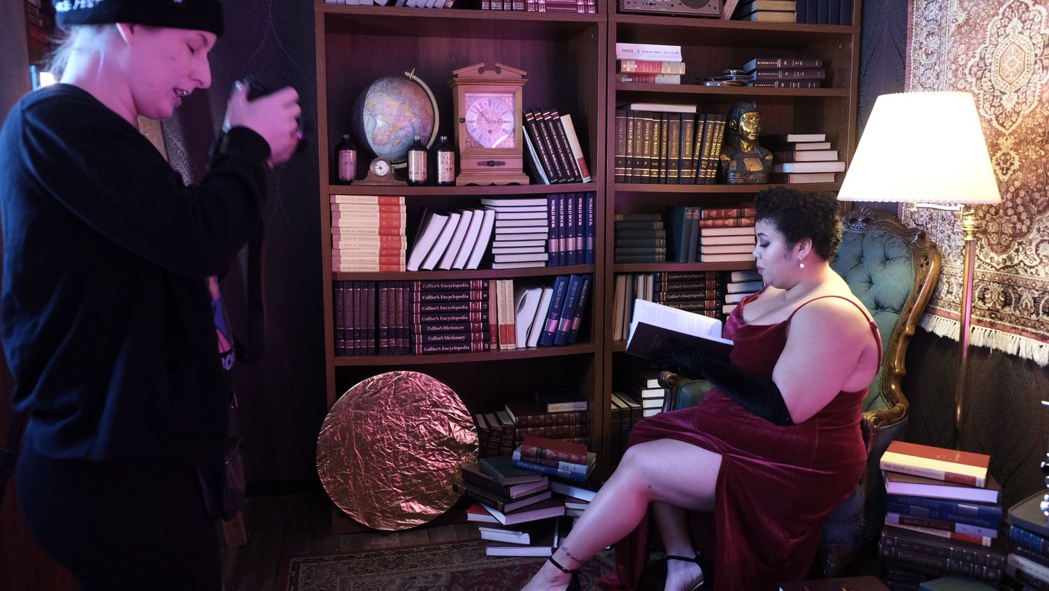 Moody library photoshoot scene with pink lighting and vintage decor elements.