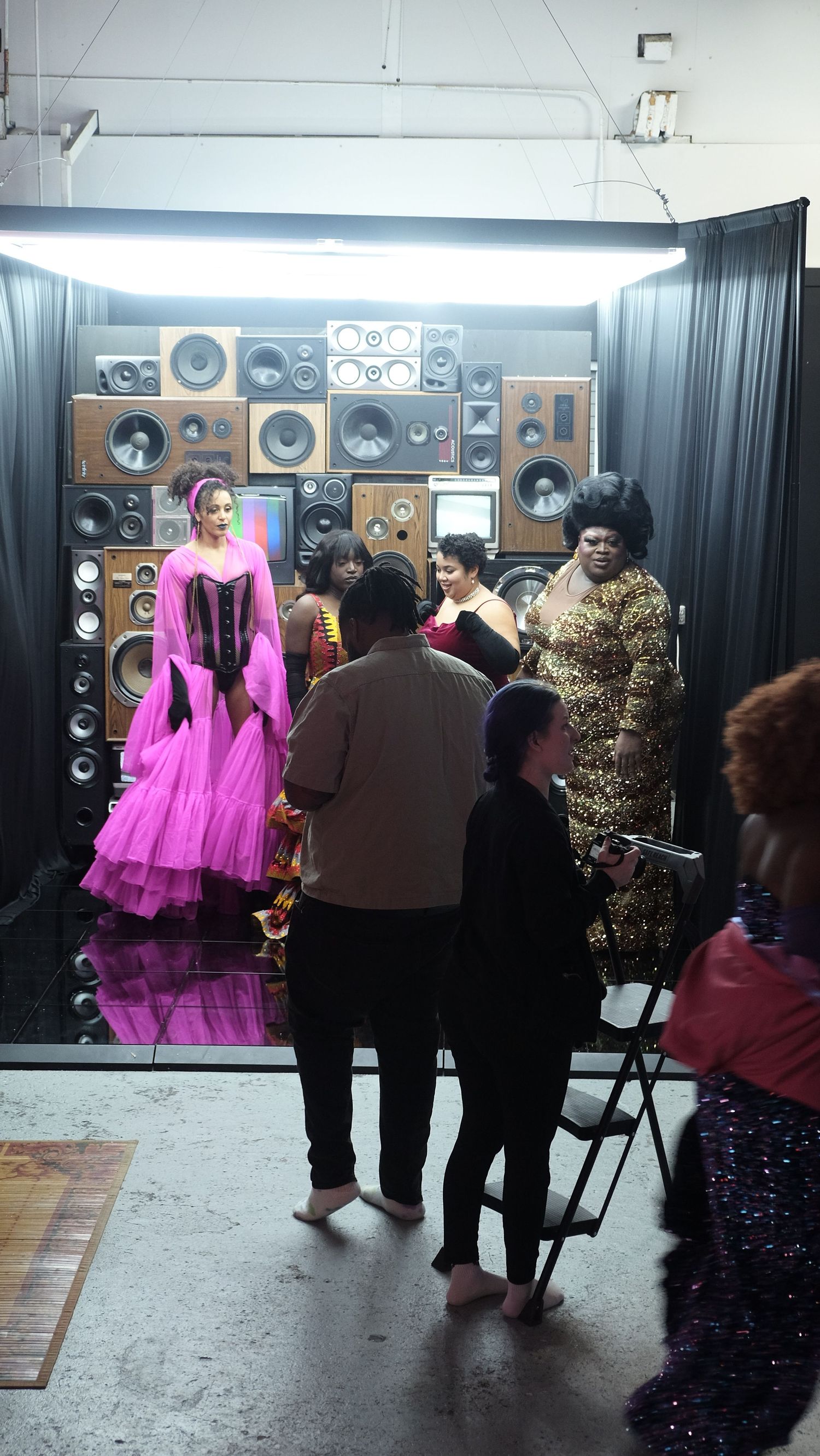 Photography session in progress with speakers wall backdrop and pink formal dress in focus.