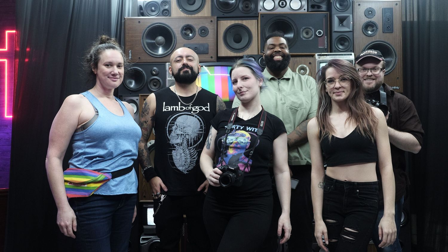 Group photo of performers and crew in front of speaker wall with neon lighting.
