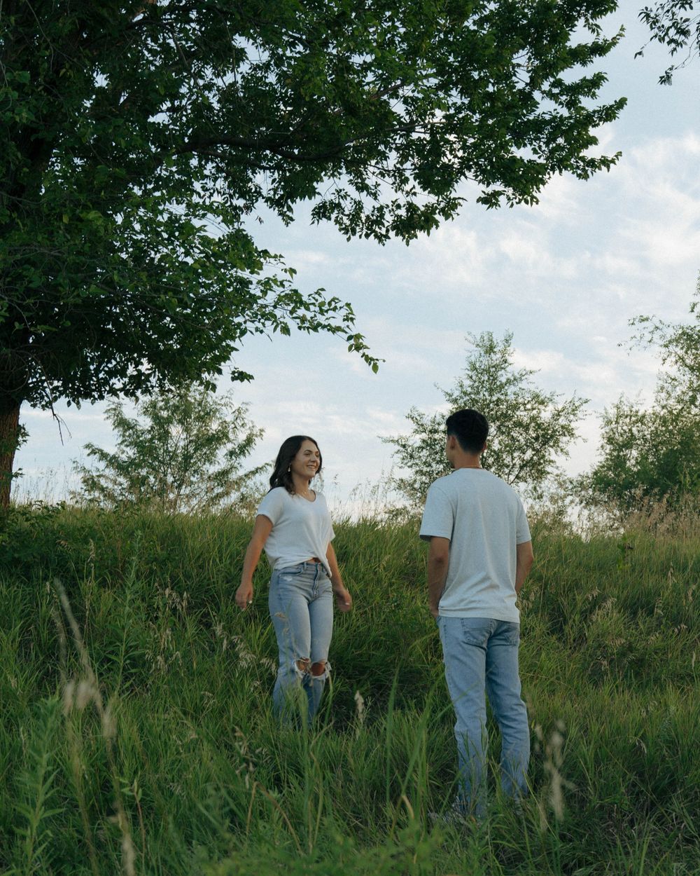 Couple standing in tall grass field with trees in background.