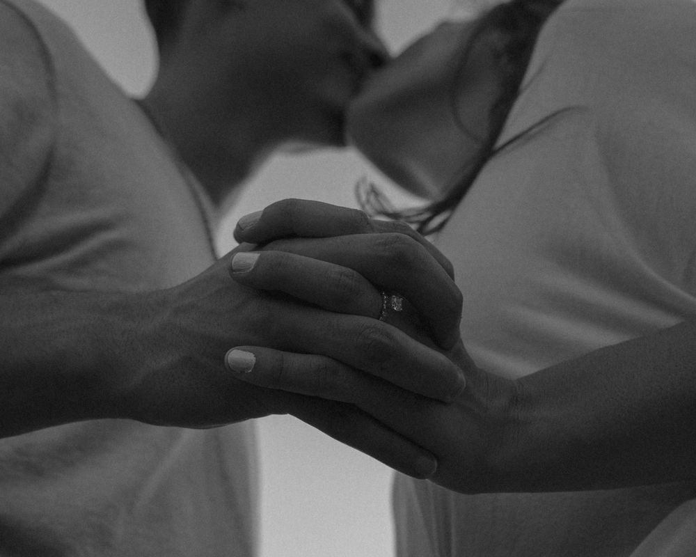 Black and white photo of hands gently holding each other with rings visible.