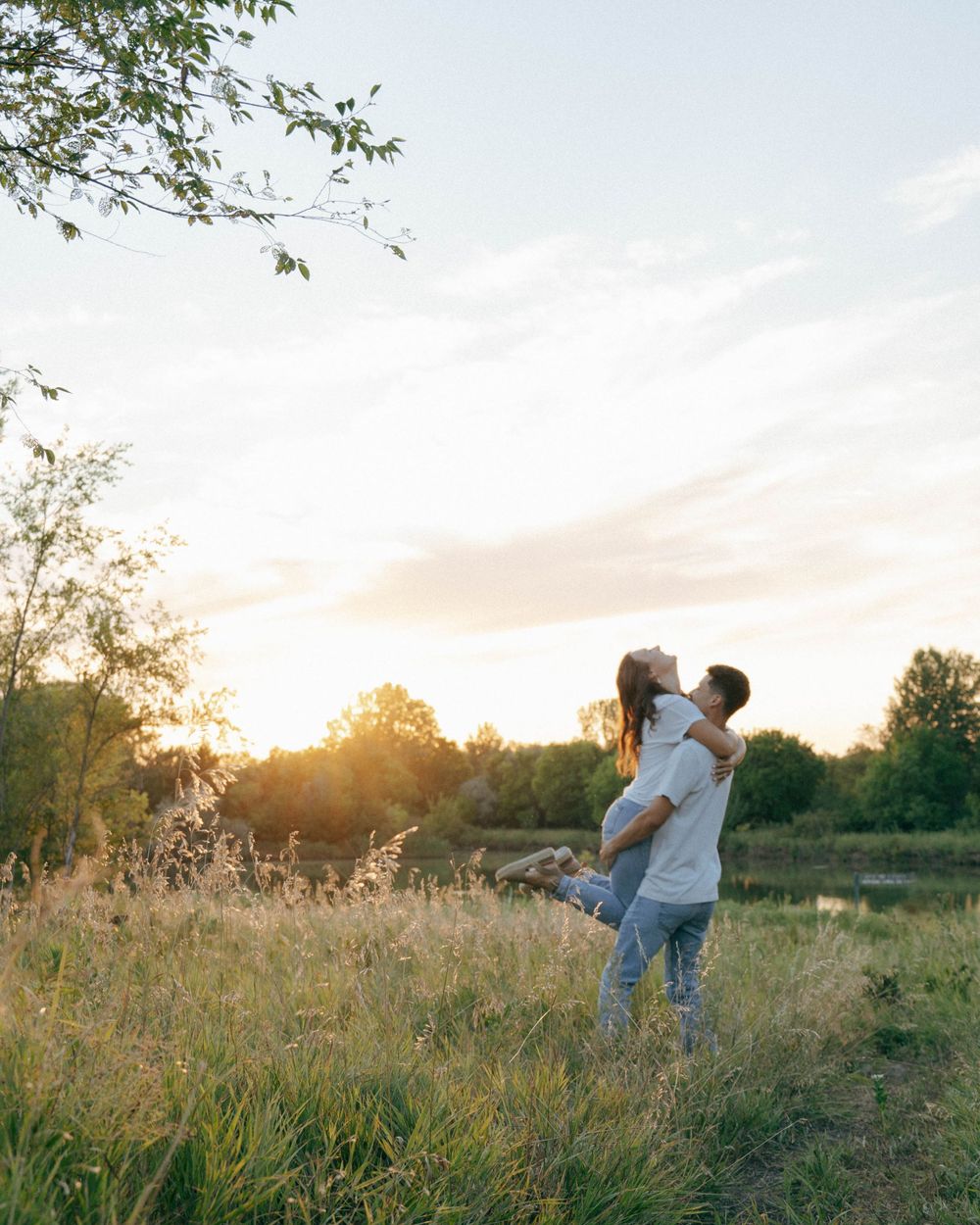 Couple sharing a joyful moment in a meadow at sunset with trees silhouetted in background.