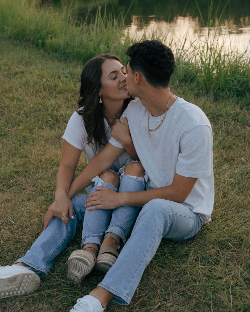 A couple sharing a tender moment while sitting by a lake during golden hour.