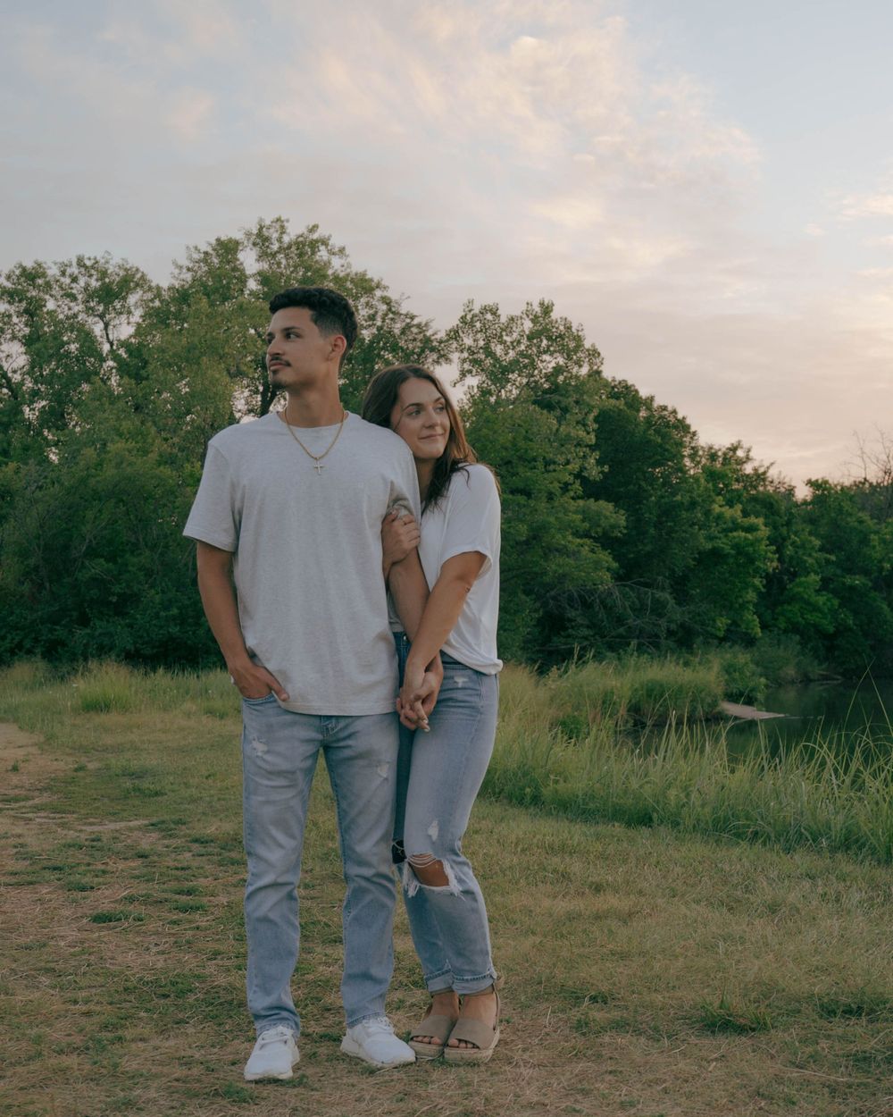 A couple in matching outfits posing playfully in a scenic outdoor setting at sunset.