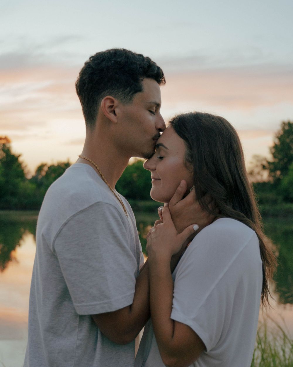A romantic couple sharing an intimate moment by a lake during golden hour.