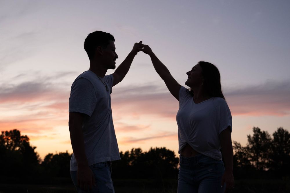 A couple dancing together in silhouette against a vibrant sunset sky.