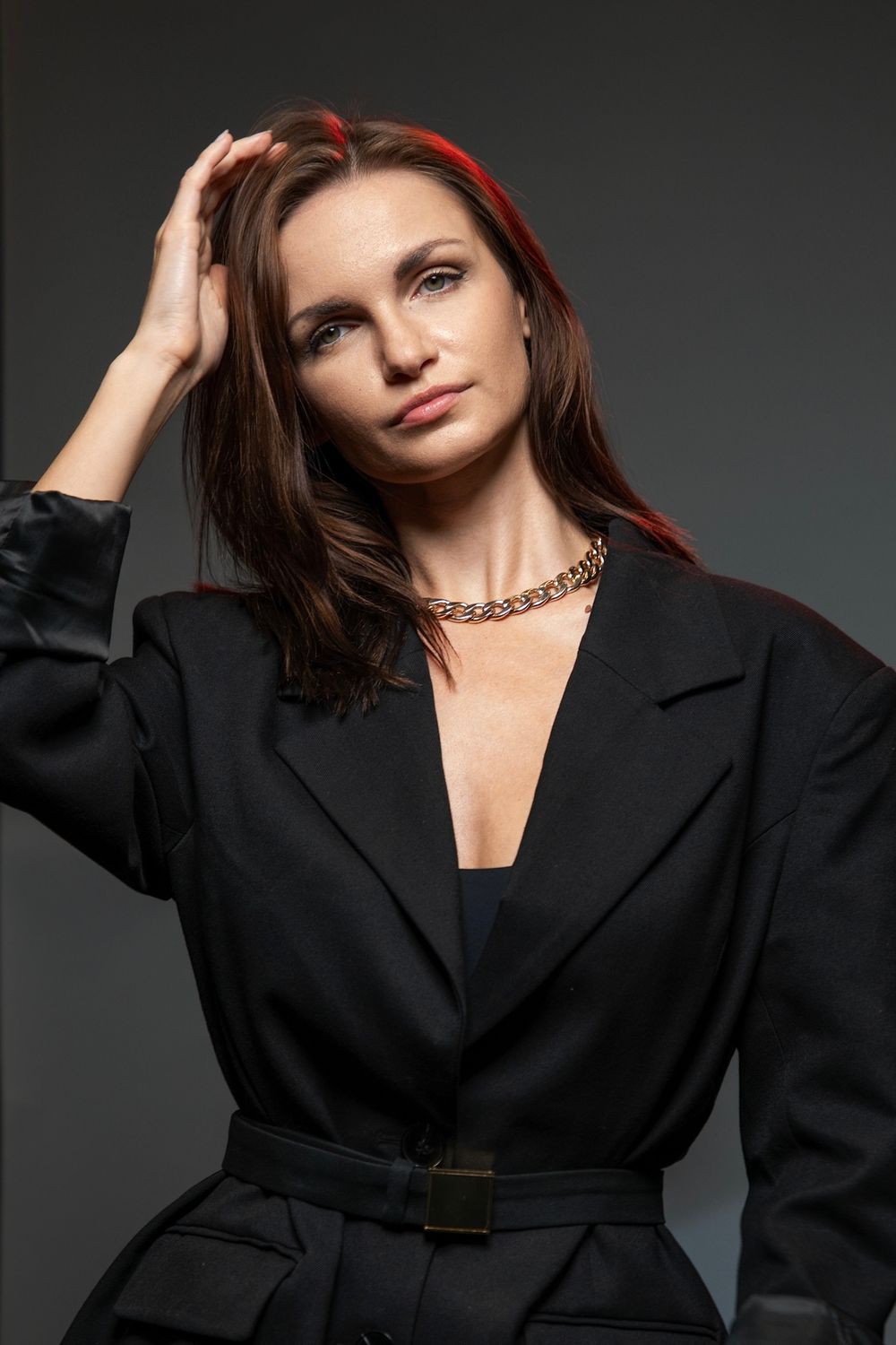 Studio fashion portrait of model in black oversized blazer with gold chain necklace.