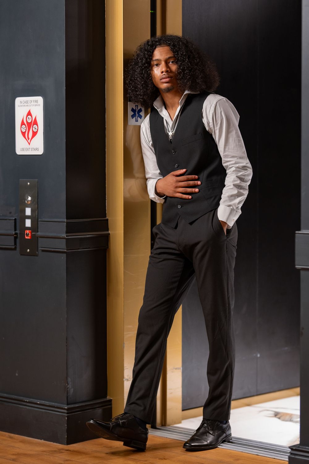 A formal business attire detail shot showing black dress pants and vest with white shirt against a dark hallway setting.