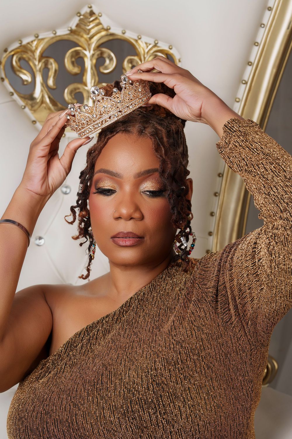 A person in a brown textured sweater poses expressively against an ornate gold-framed background.