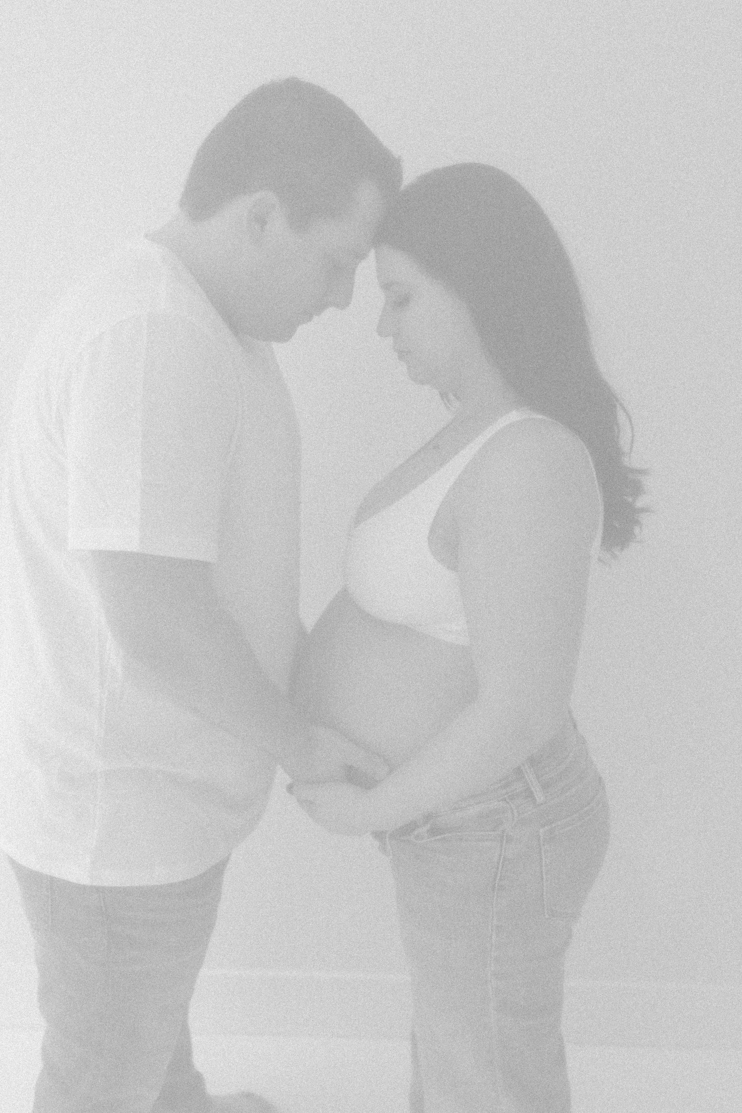 A soft, high-key maternity photo capturing an intimate moment between expectant parents.
