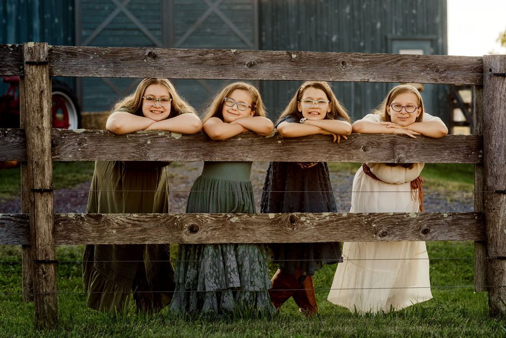People posing playfully behind a rustic wooden fence on a farm.