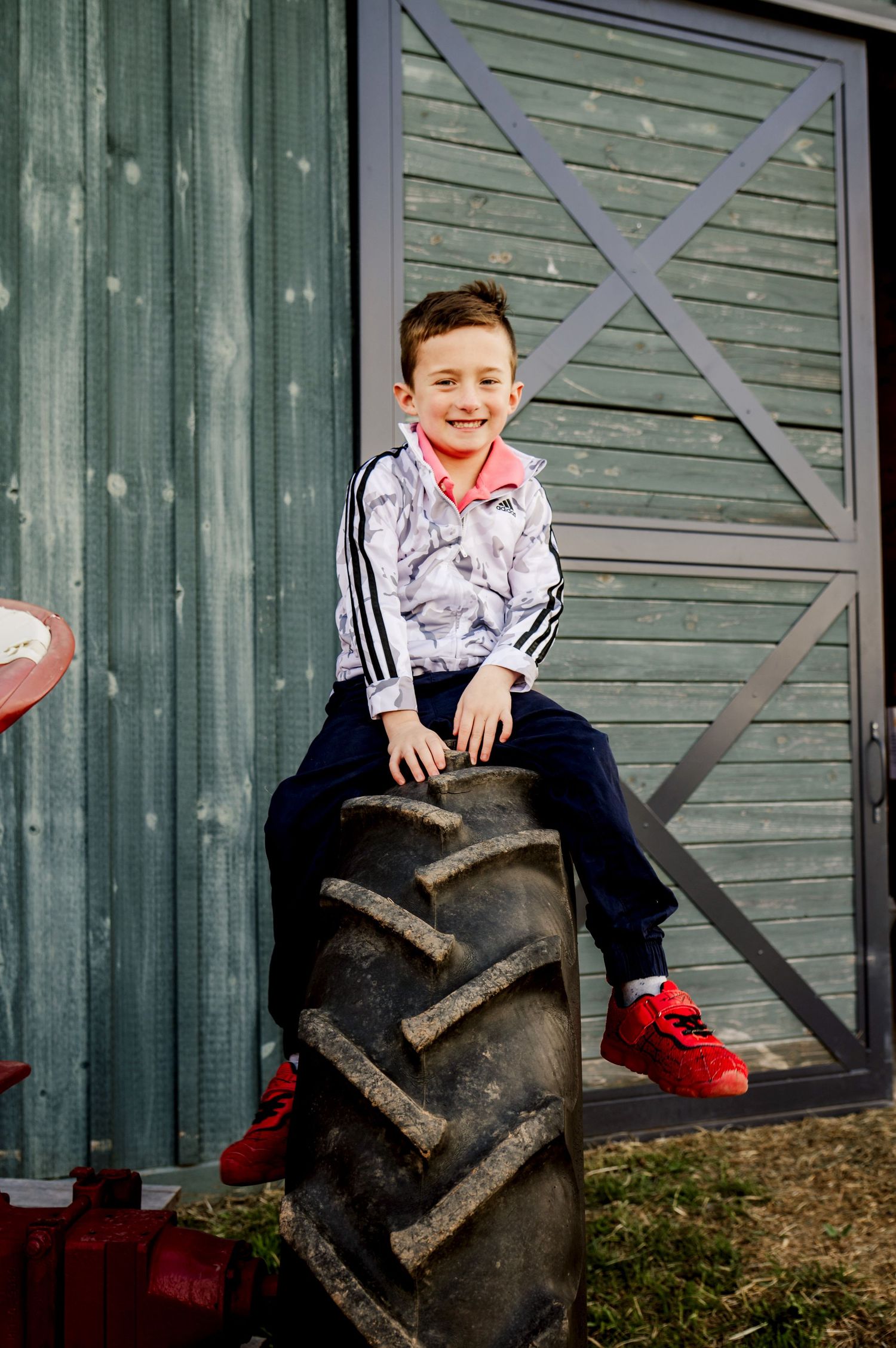 A playful scene of someone sitting on a large tractor tire against a green barn wall.