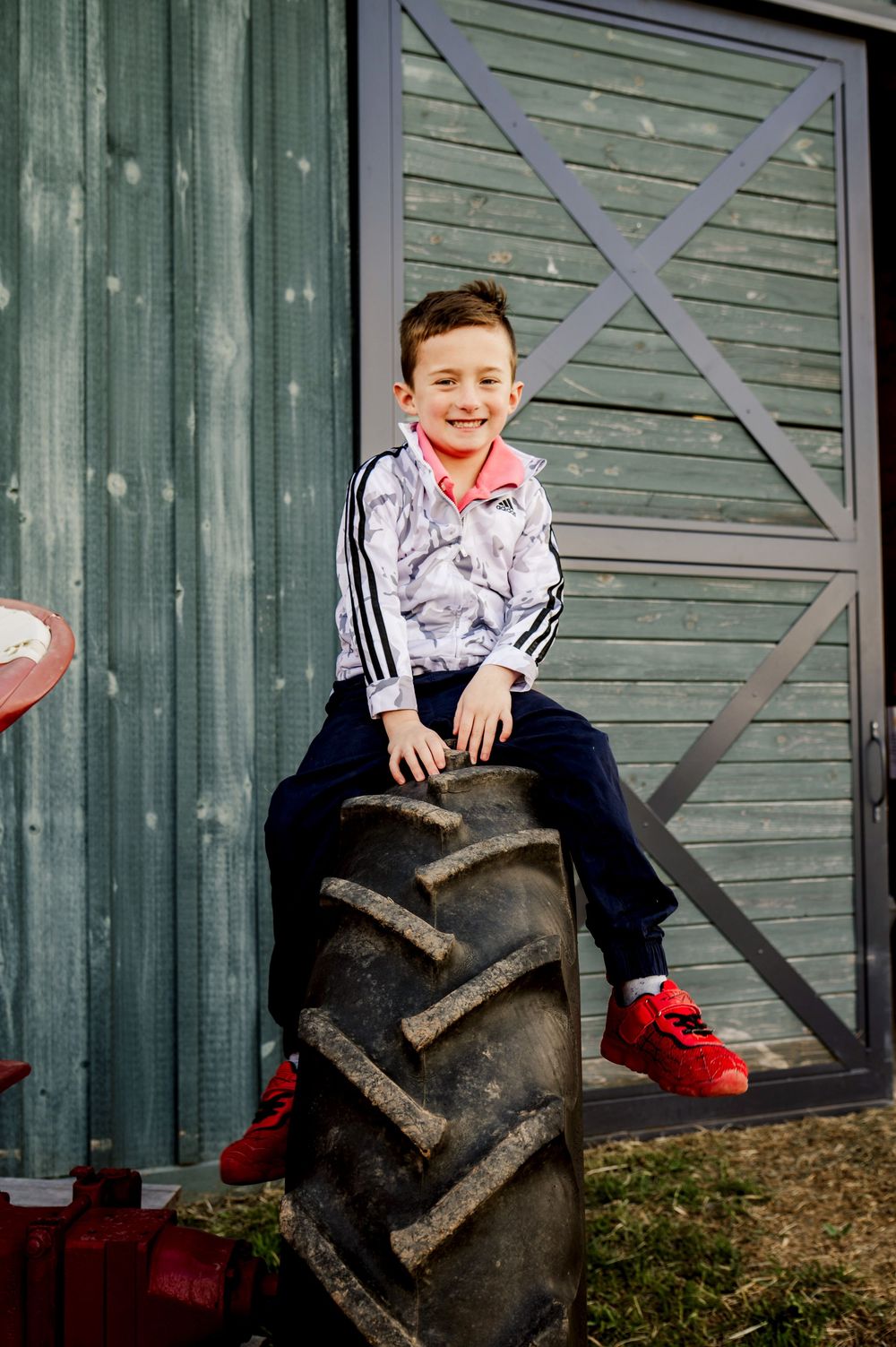 A playful scene of someone sitting on a large tractor tire against a green barn wall.