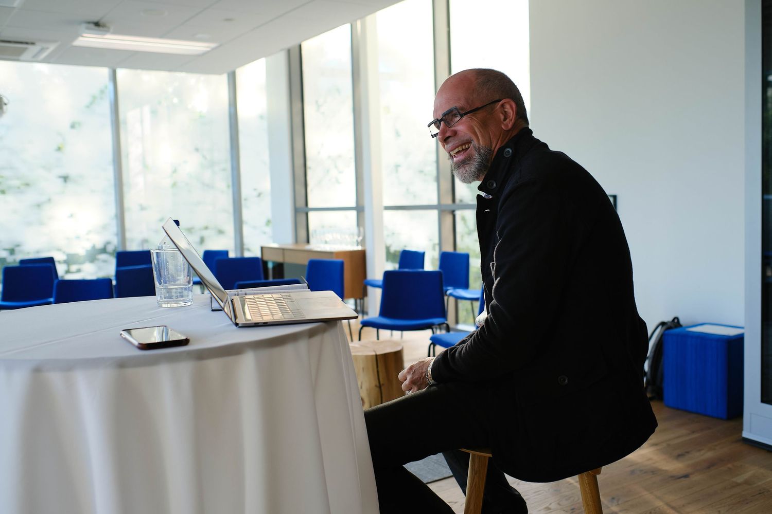 Professional working at laptop in bright conference room with blue chairs.