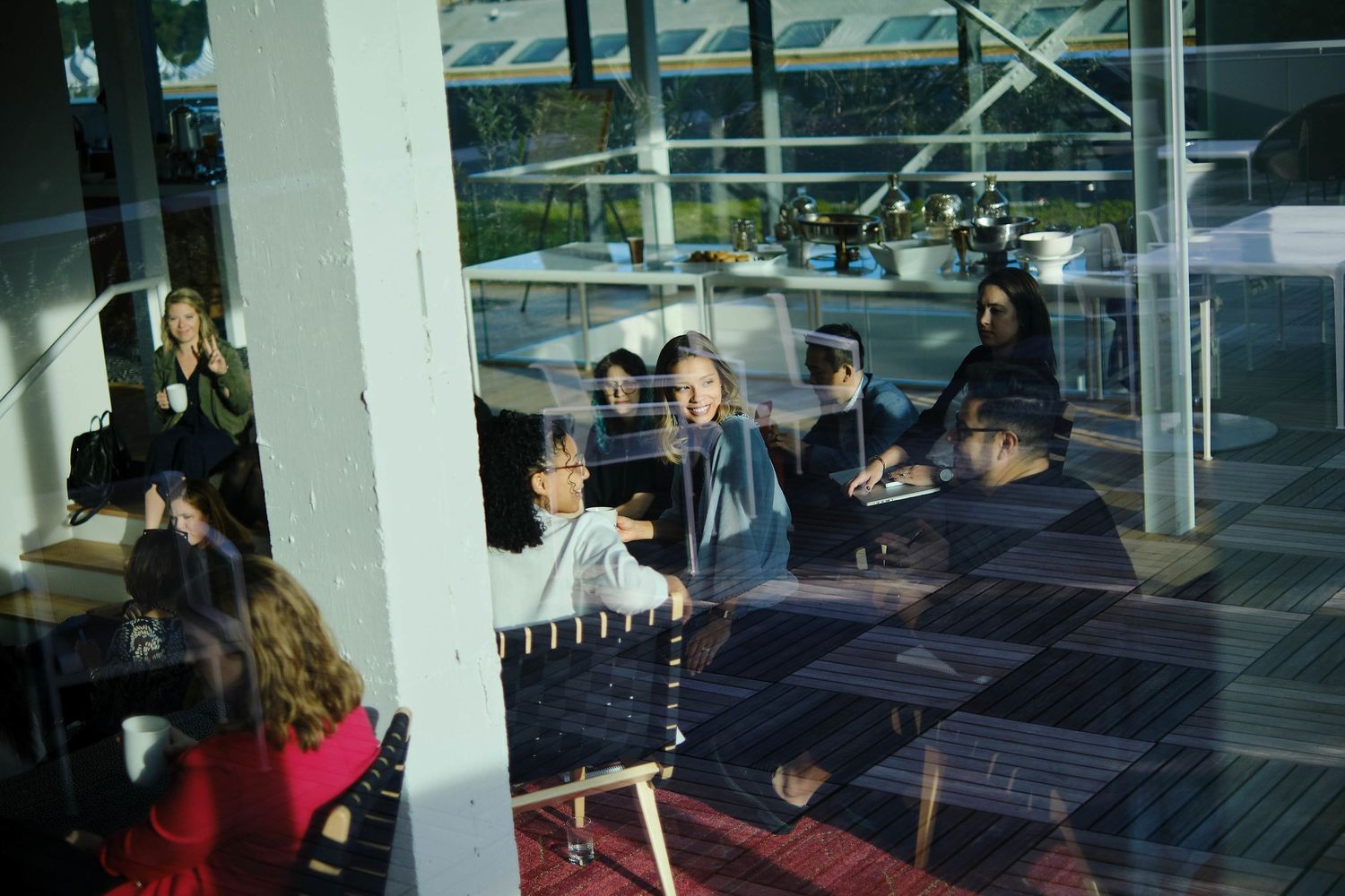 Group gathered around tables in bright modern space with windows and white pillars.