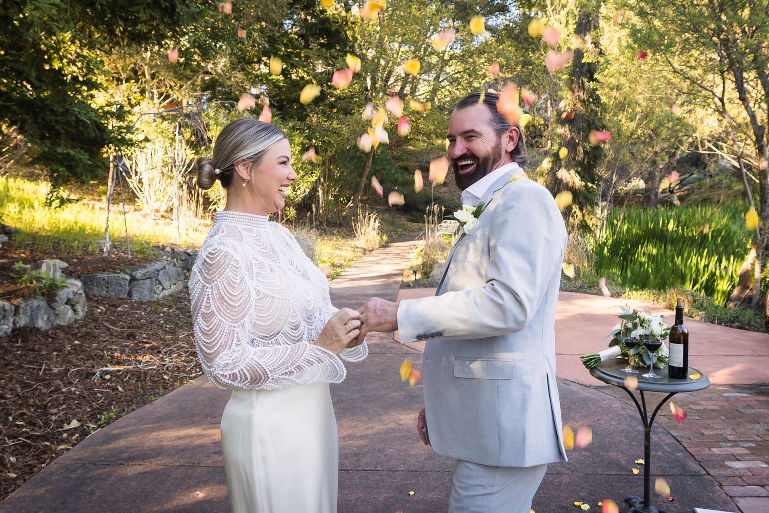 A couple shares a romantic moment during their outdoor wedding ceremony in a sunlit garden setting.