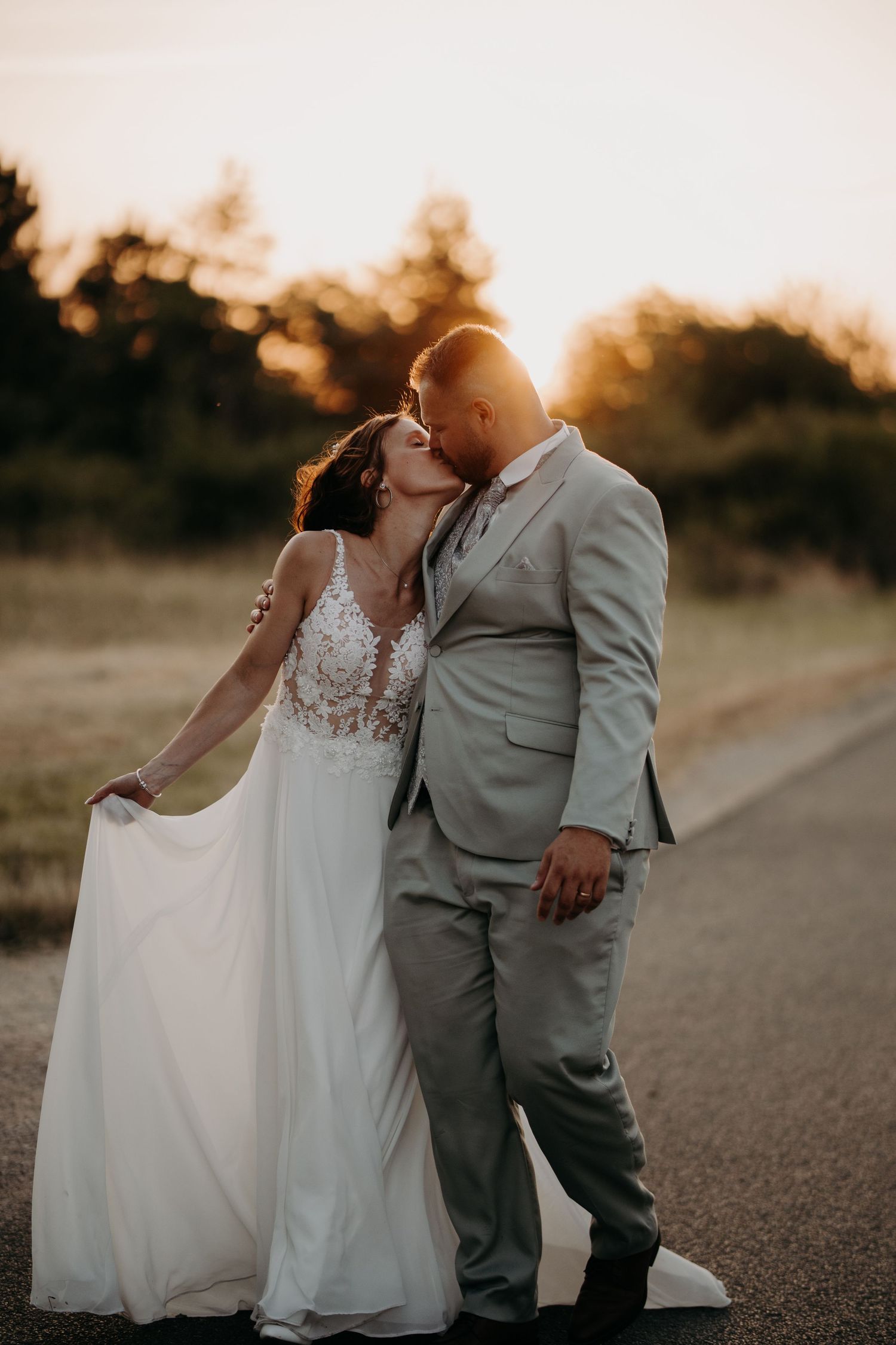 A couple shares an intimate moment at sunset in formal wedding attire.