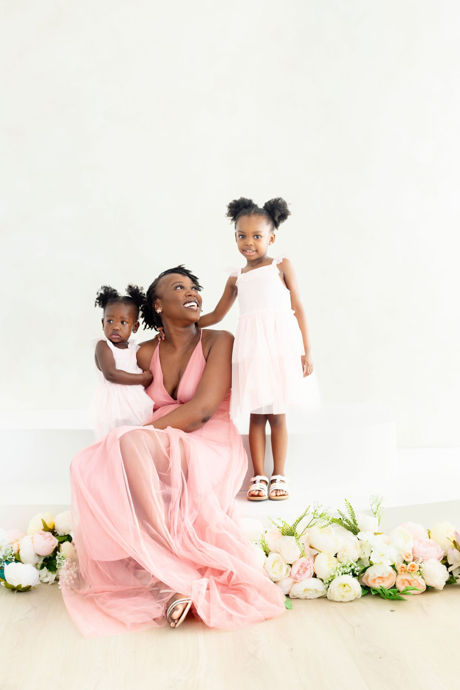 A child in a pink dress poses playfully on a white floor with floral decorations.