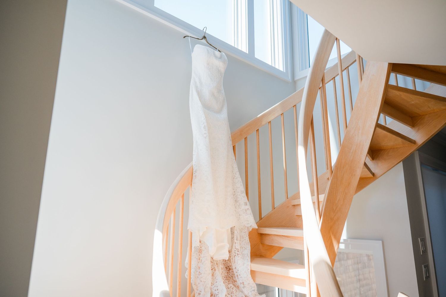A bright and airy hallway with white walls features a wooden staircase and natural light streaming through windows.