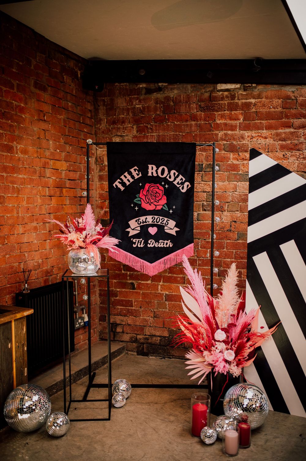 Modern event space with exposed brick walls, black and white striped decor, and pink dried floral arrangements.