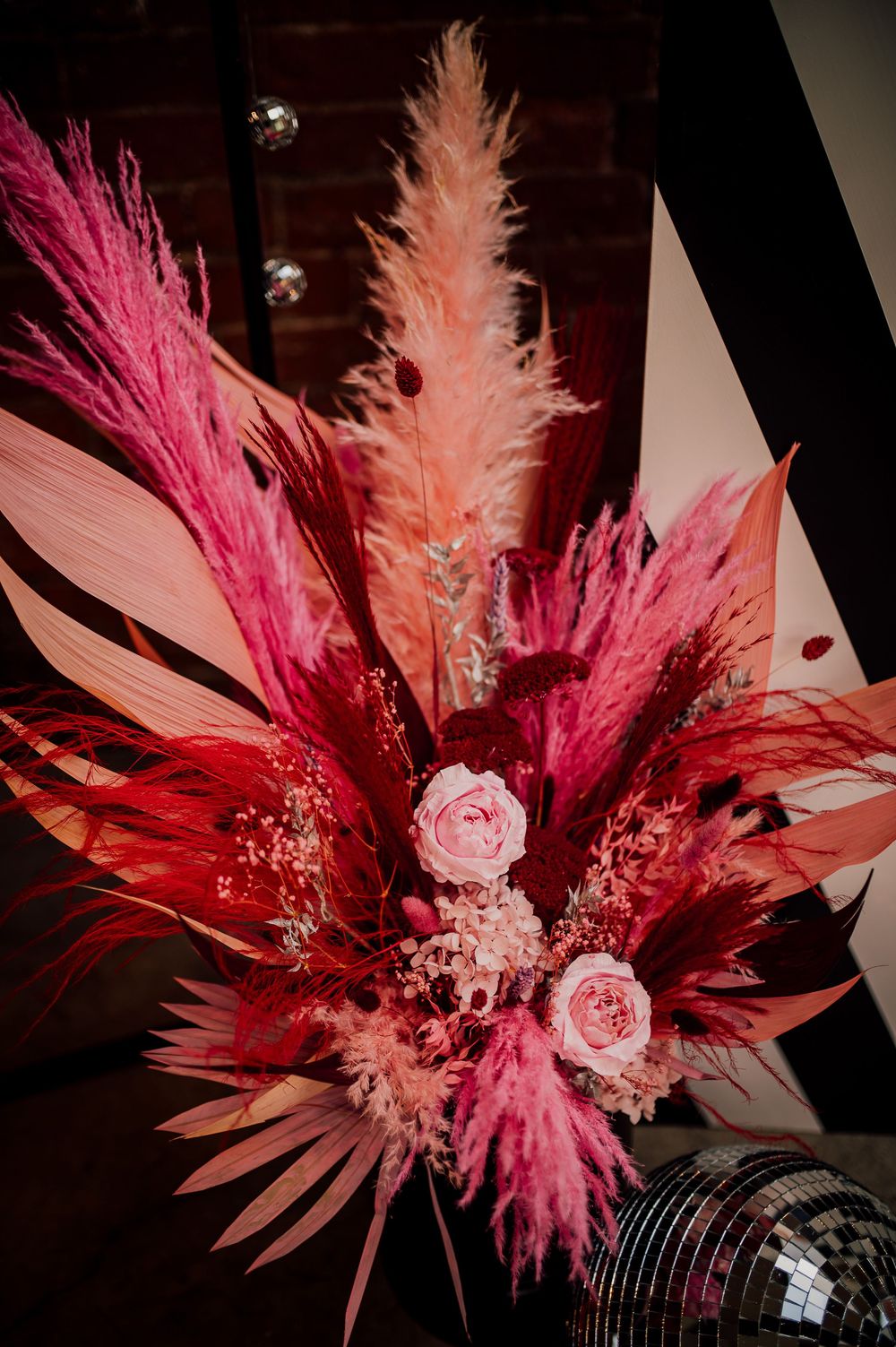 A series of pink and red dried floral arrangements with pampas grass and roses against a dark background.