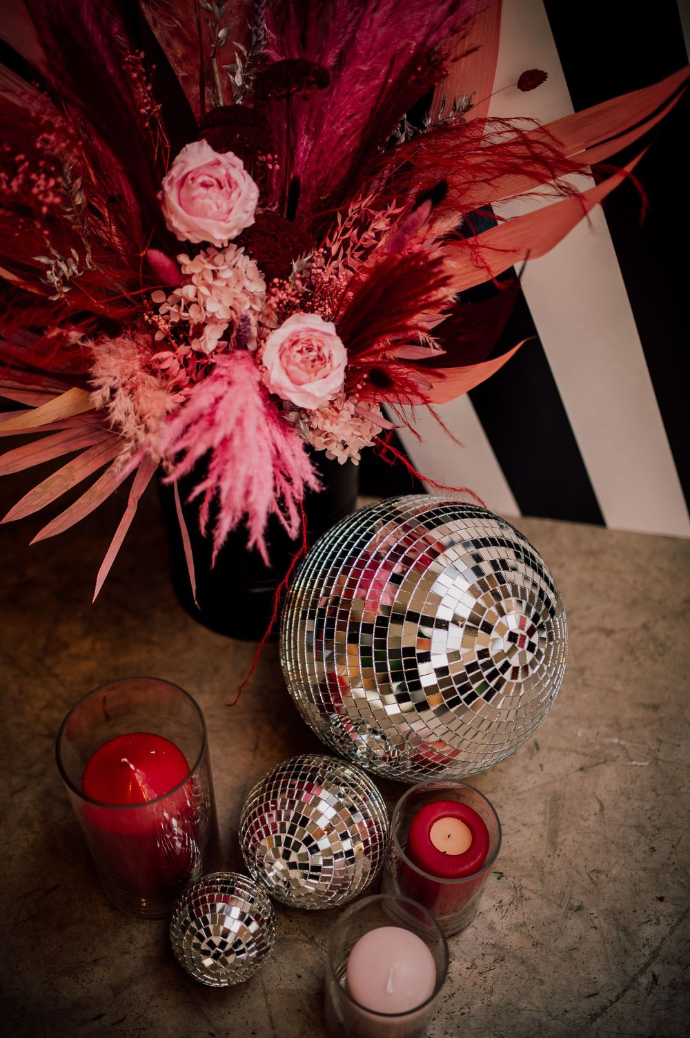 Disco balls and candles create a romantic pink and red party atmosphere with dried flowers and palm fronds as decor.