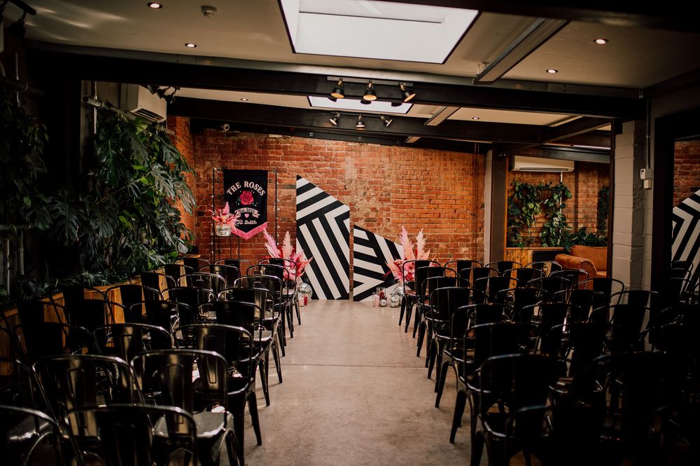 Interior view of a dimly lit restaurant with exposed brick walls and black chairs arranged in rows for an event setup.