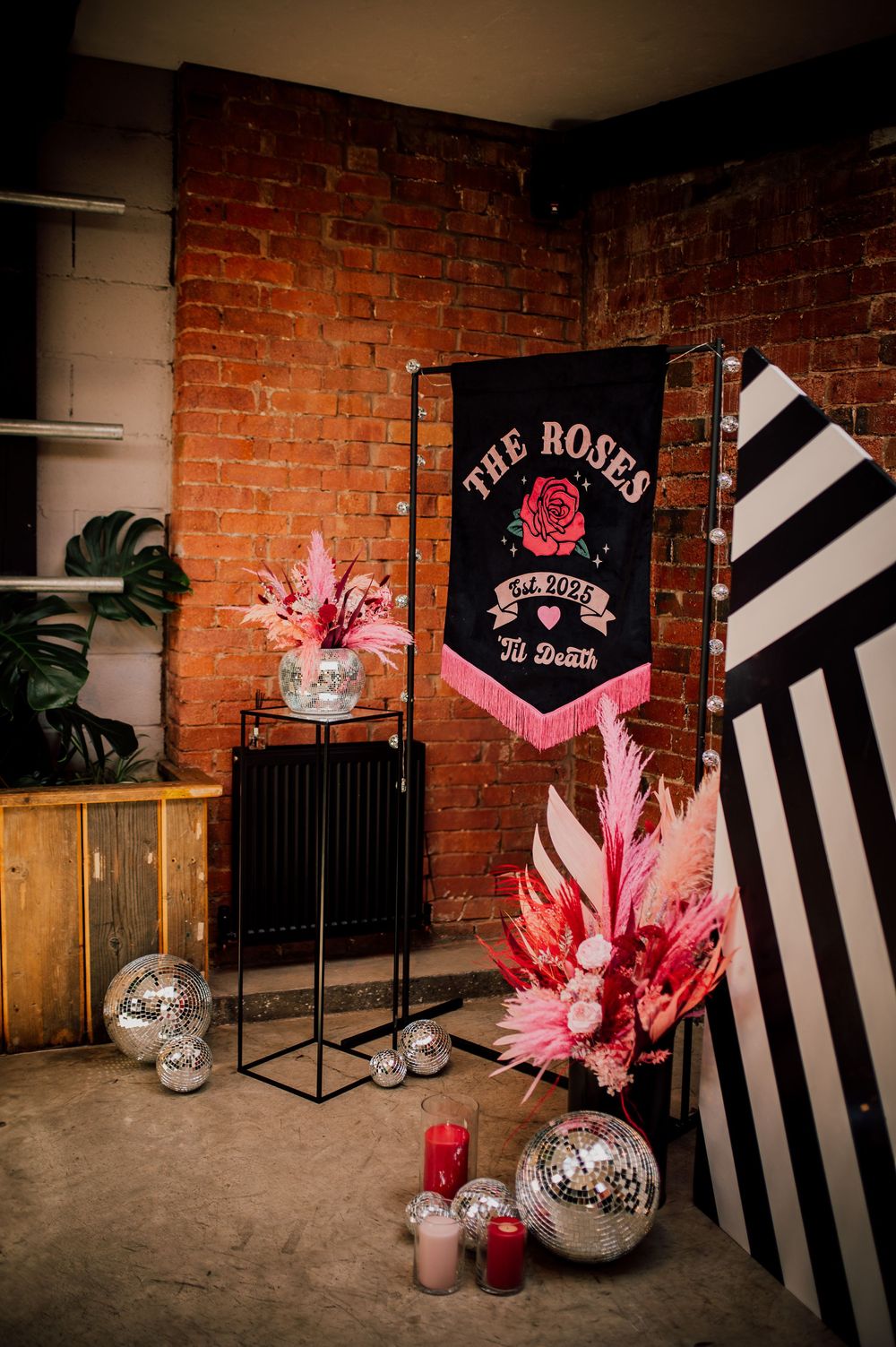 Stylish event setup with black and white striped backdrop, pink floral arrangements, and neon signage against exposed brick walls.