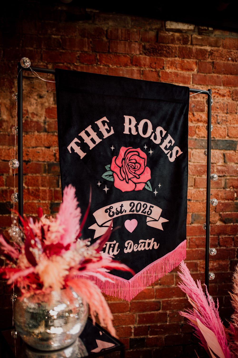 Pink floral decorations and signage with 'The Rose' text against exposed brick walls in a rustic venue setting.
