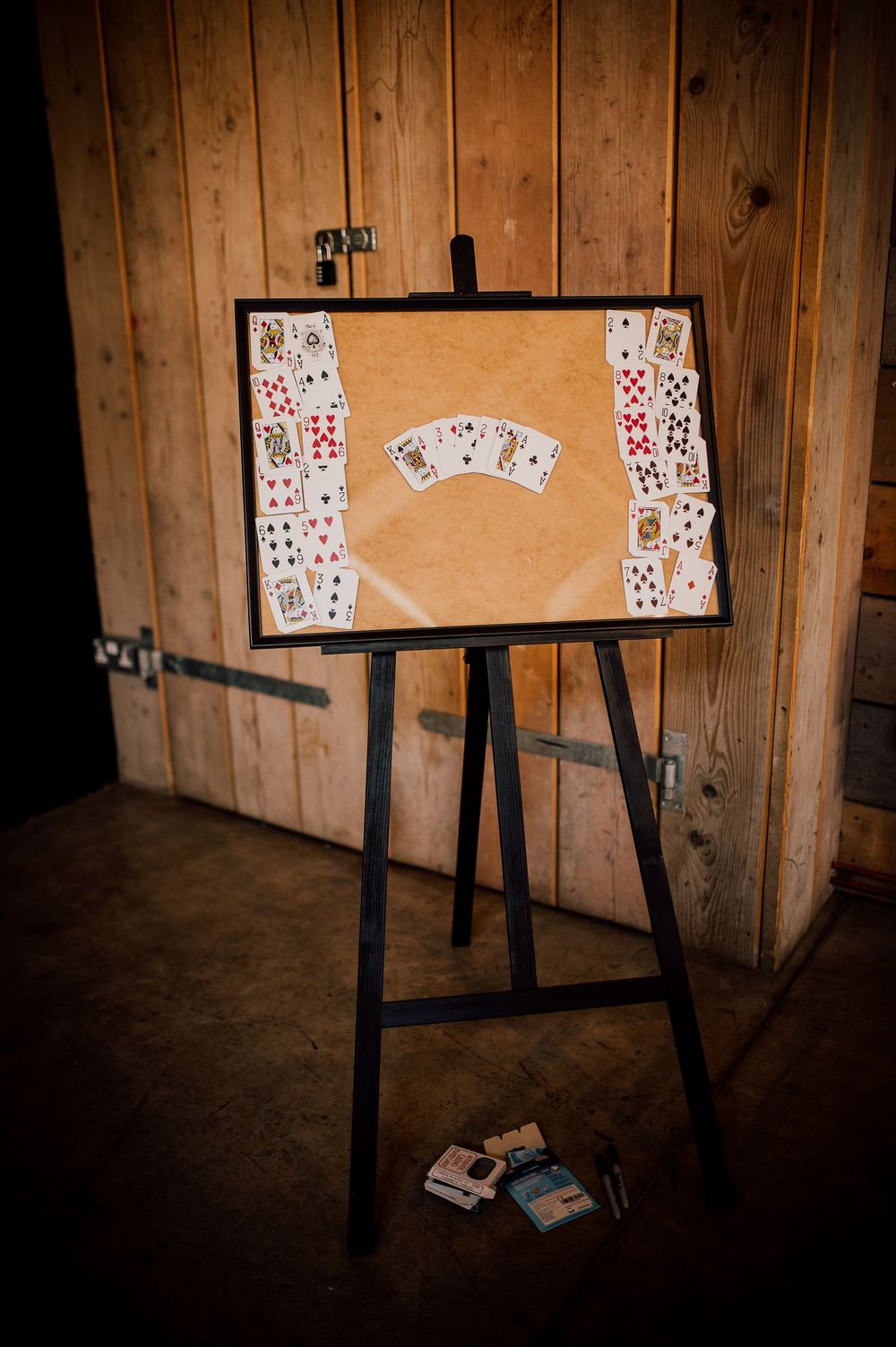 Playing cards arranged in a sequence on a wooden board against rustic wooden wall panels in dim lighting.