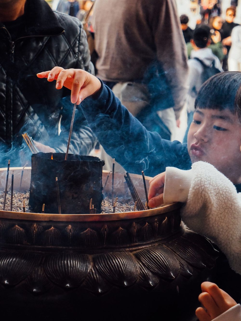 Smoke rises from an incense burner at a Japanese temple as visitors gather around.