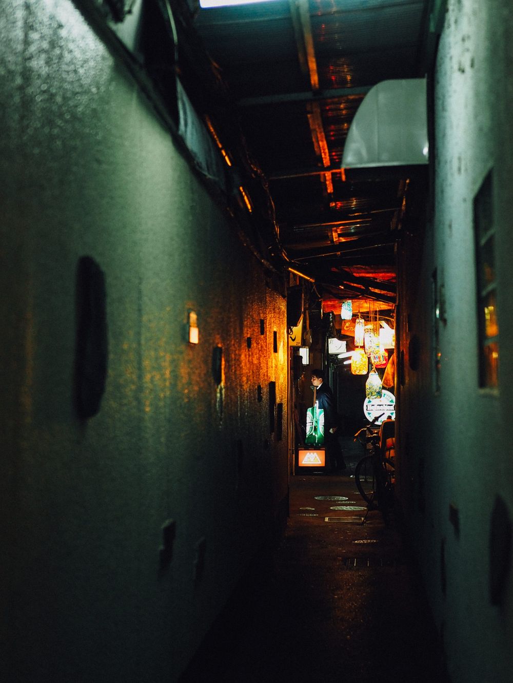 A dimly lit narrow alleyway in Japan with glowing lanterns and neon signs creating an atmospheric mood.