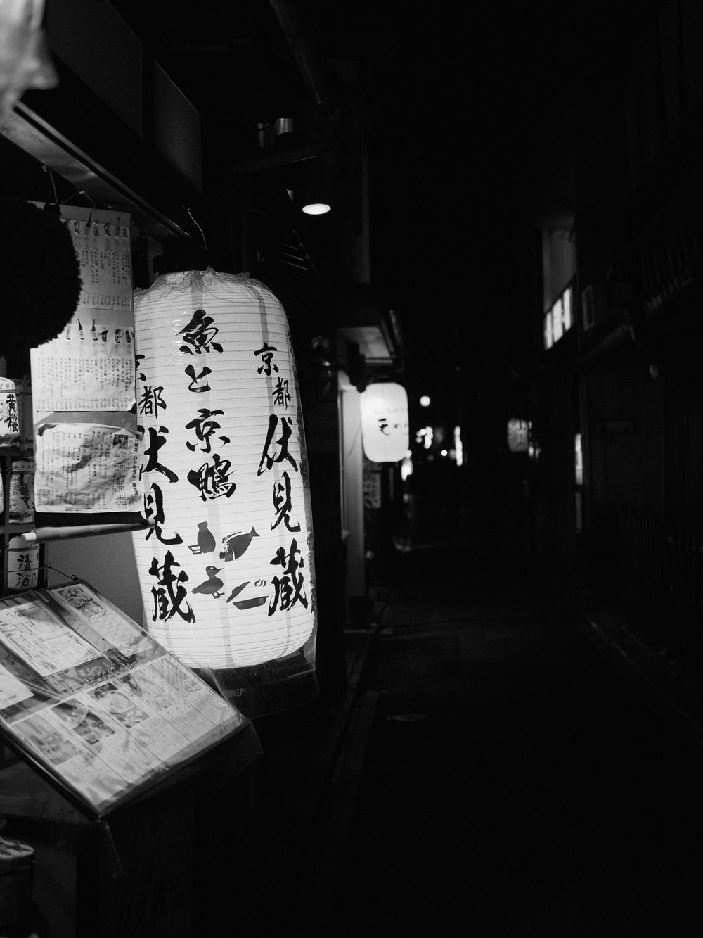 Traditional Japanese paper lanterns with calligraphy illuminated in a dark alley.