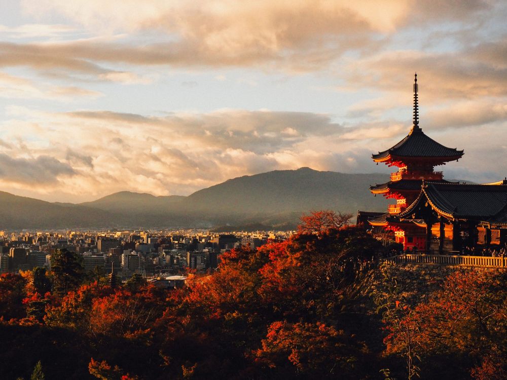 Traditional Japanese pagoda silhouetted against a dramatic sunset sky with autumn foliage in the foreground.