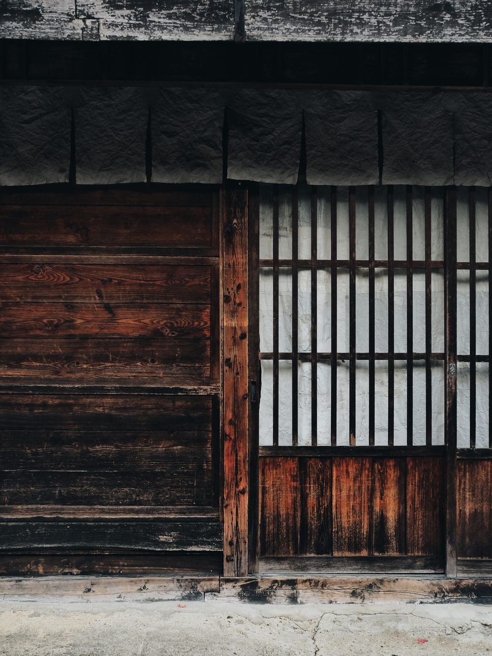 Traditional Japanese architectural detail showing wooden panels and shoji screen windows with dark textured walls.
