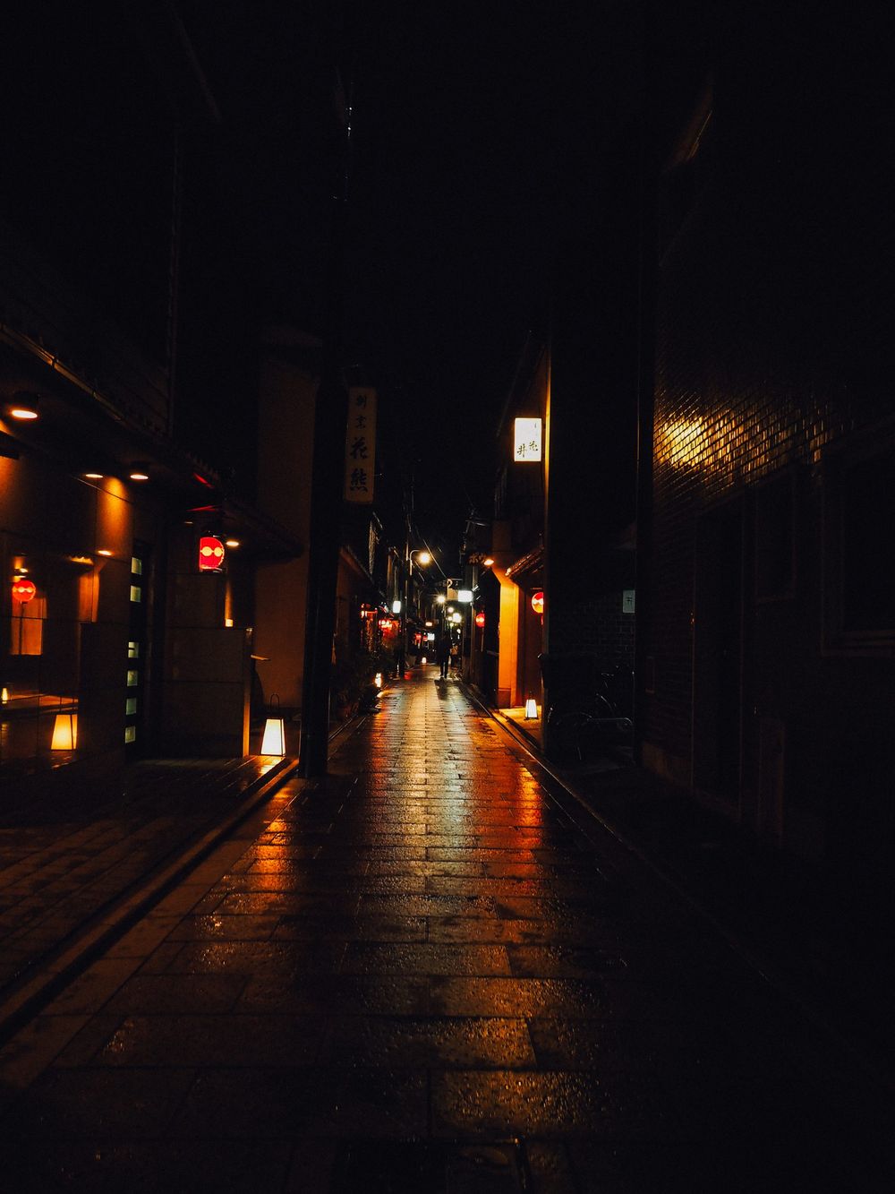 Atmospheric night scene of a traditional Japanese street with warm lantern lighting reflecting on wet stone.
