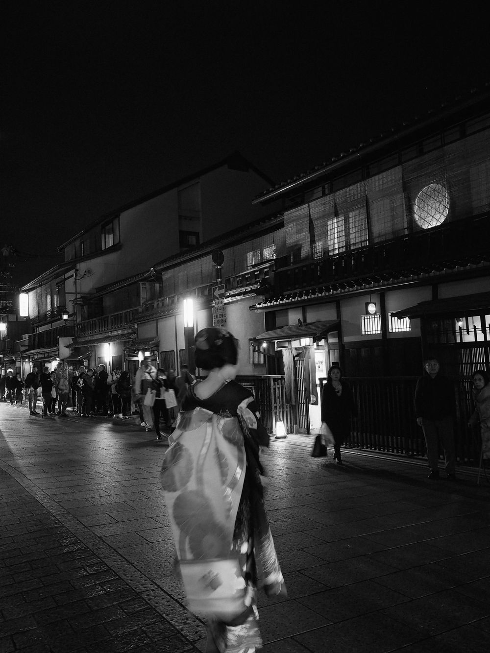 Night scene of illuminated traditional Japanese buildings with street lights casting warm glows.