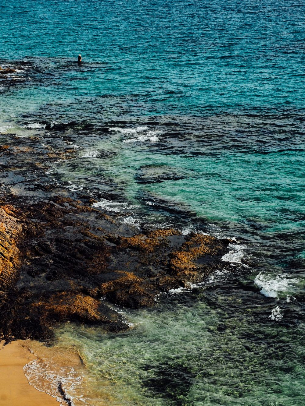 Turquoise ocean waters meeting rocky coastal cliffs with dramatic contrast.