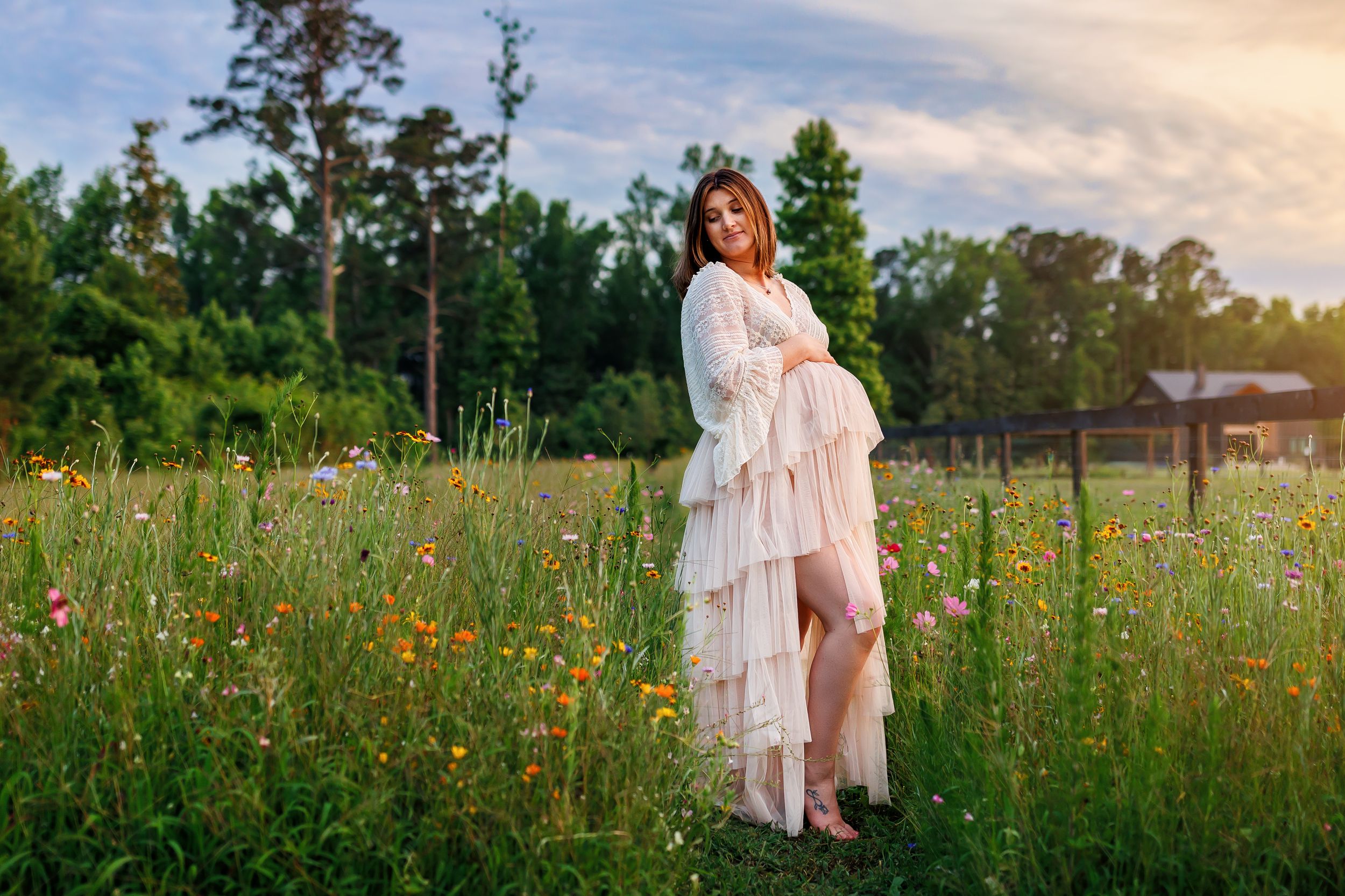 A flowing white ruffled dress stands out against a wildflower meadow at sunset with trees in the background.