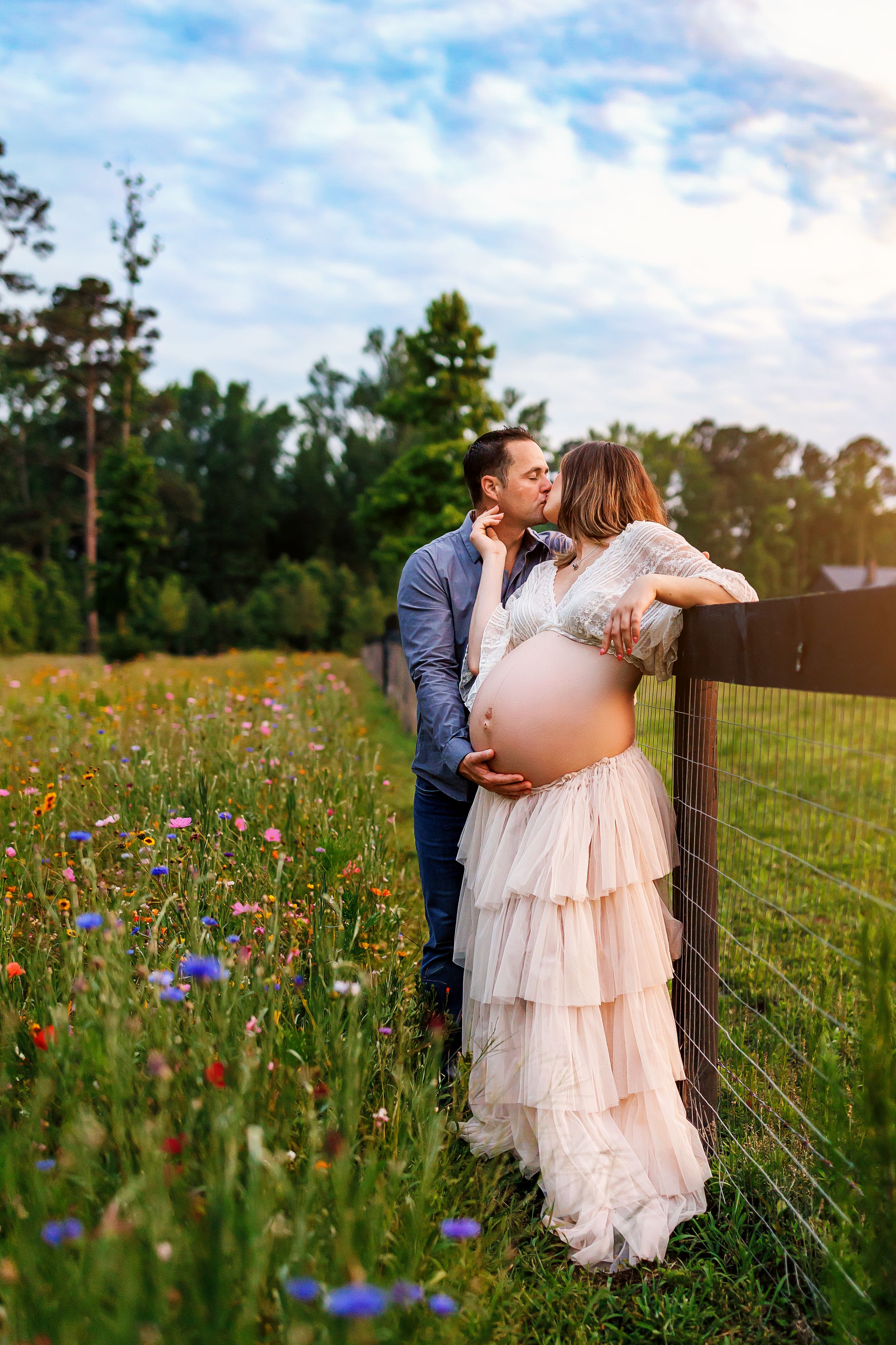 A couple shares a romantic moment in a wildflower meadow wearing blush pink dress and navy suit at sunset.