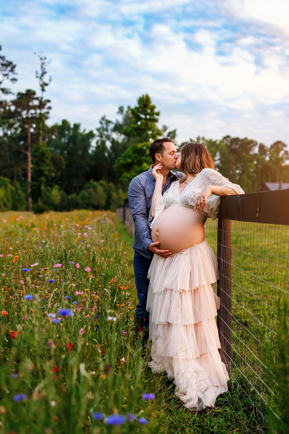 A couple shares a romantic moment in a wildflower meadow wearing blush pink dress and navy suit at sunset.