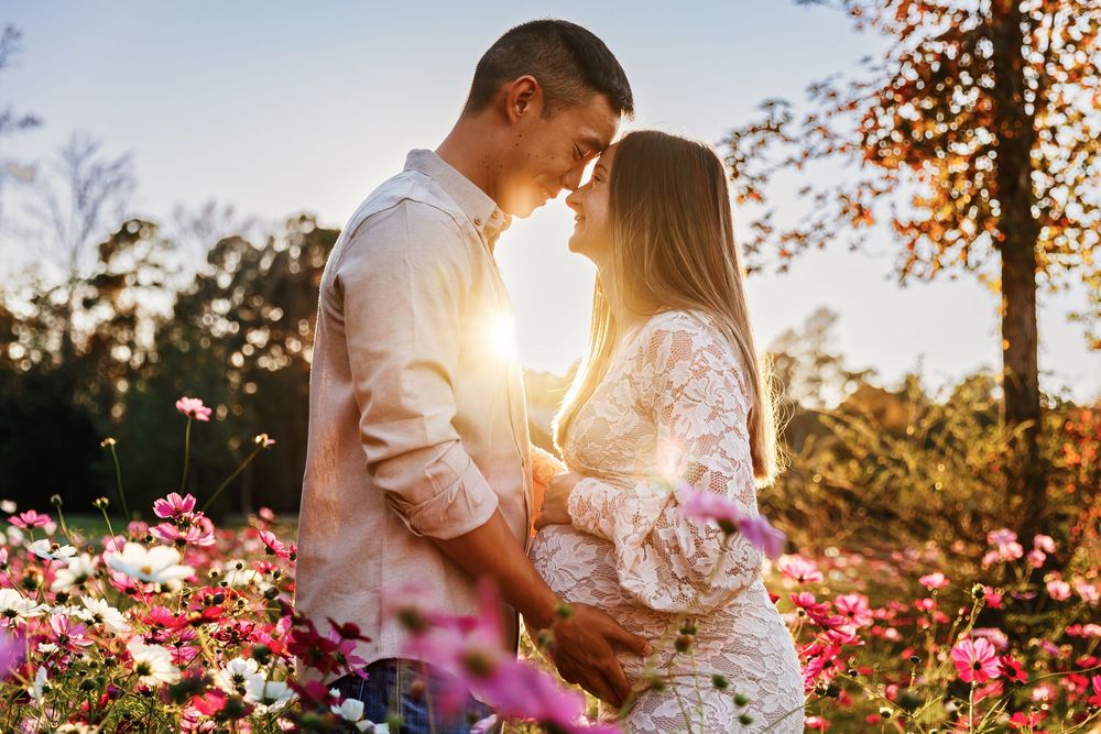 A romantic couple embraces in a flower garden at sunset with golden light streaming through autumn trees.