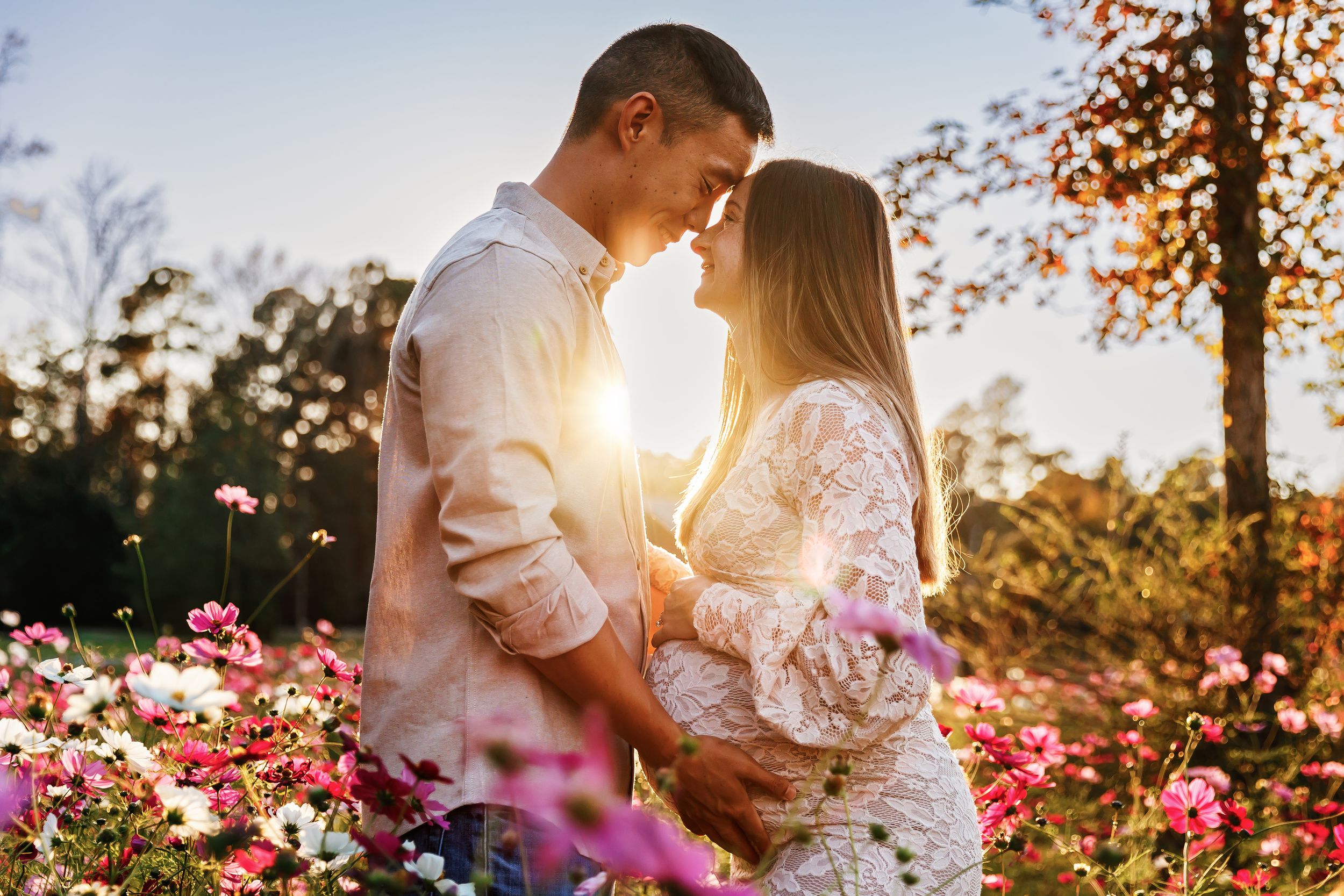A romantic couple embraces in a flower garden at sunset with golden light streaming through autumn trees.