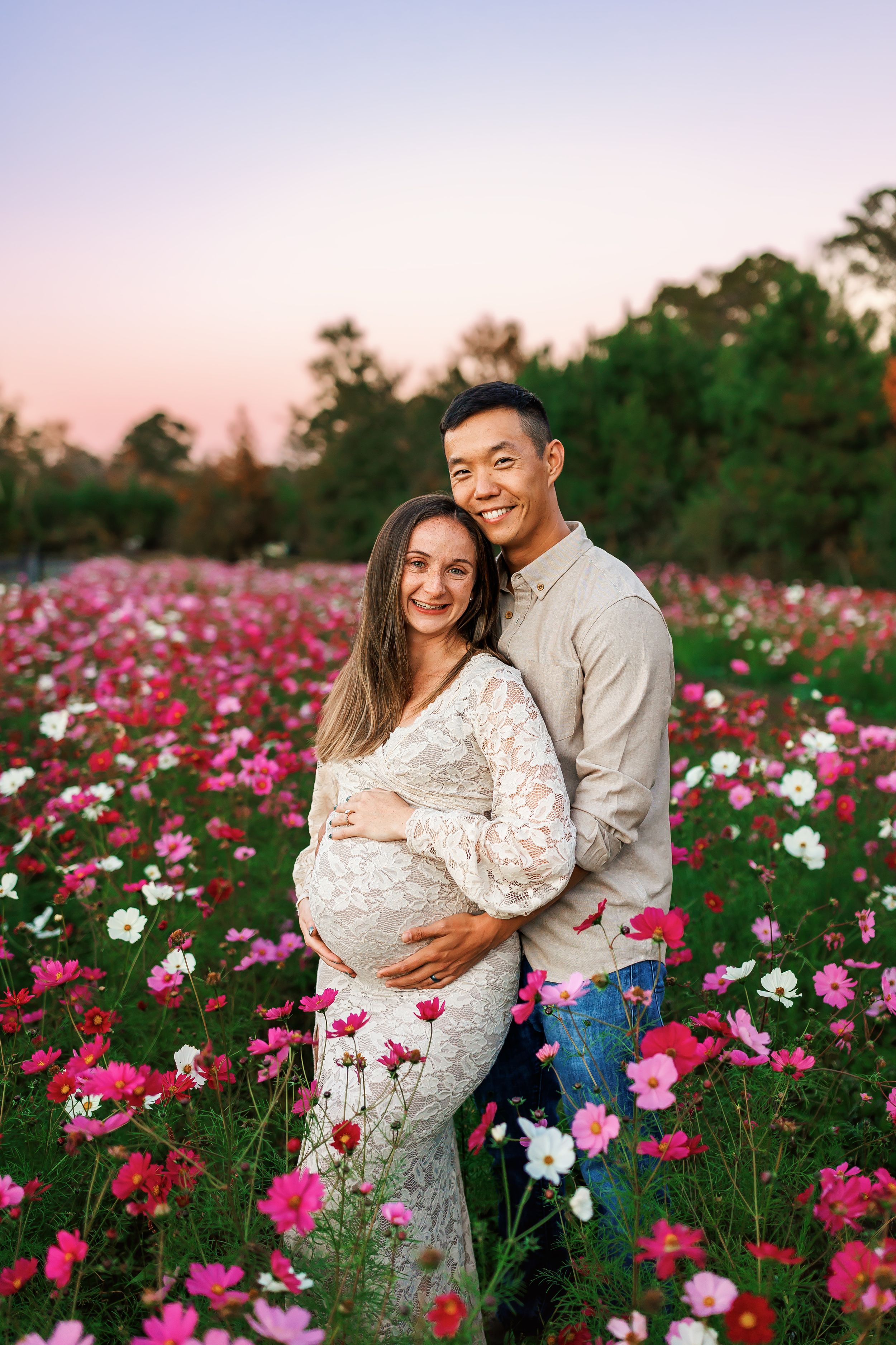 A couple shares an intimate moment in a vibrant field of pink and white cosmos flowers during sunset.